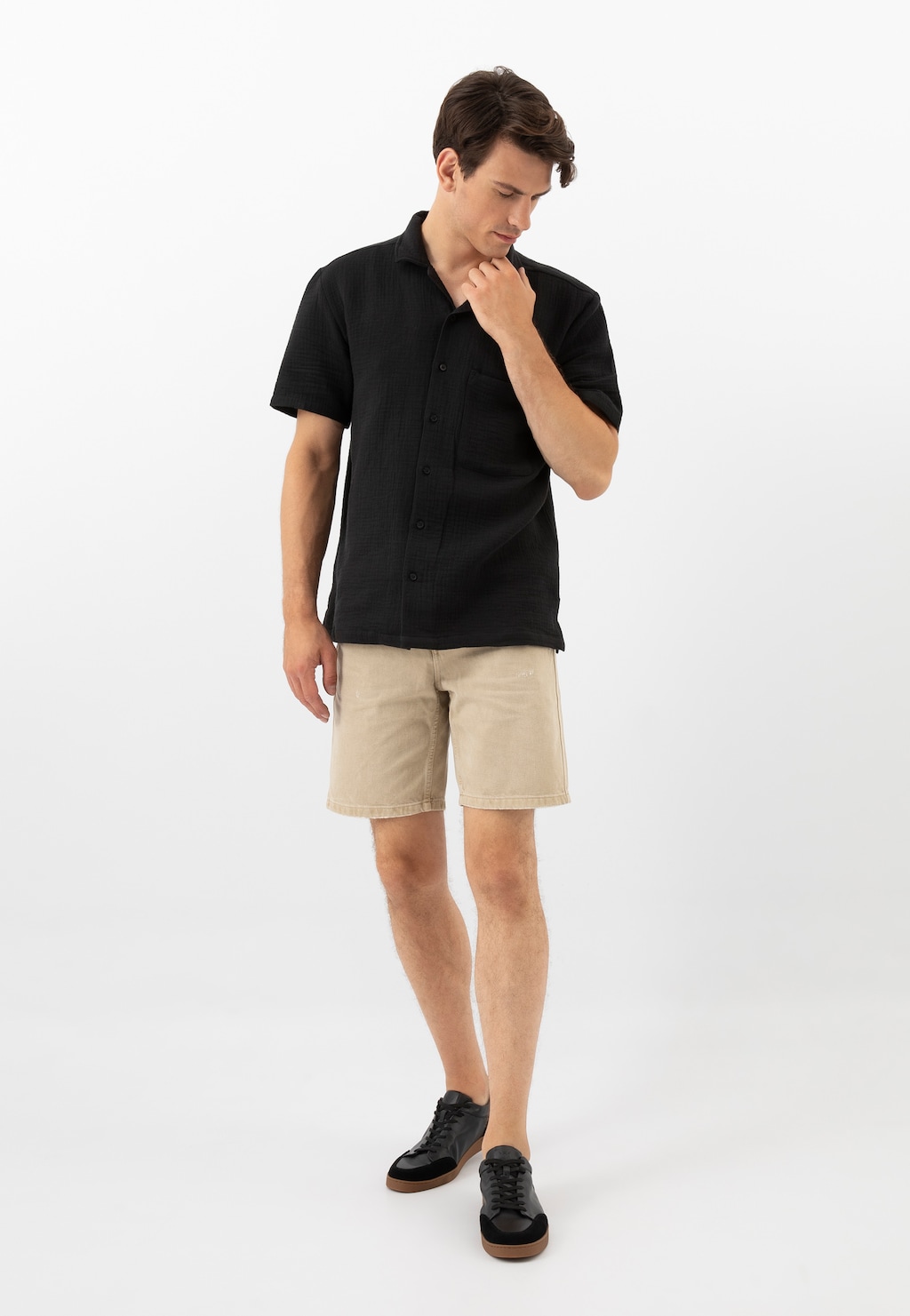 Model w czarnej koszuli i beżowych szortach prezentuje czarne trampki Wojas 10217-51 z łączonych skór na charakterystycznej brązowej podeszwie, ukazując casualowy letni look.