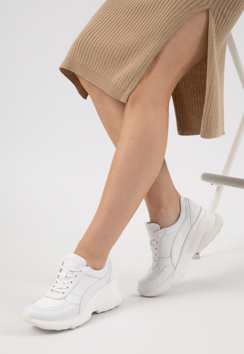Białe skórzane sneakersy damskie Wojas 46106-59 na podwyższonej podeszwie, prezentowane na modelce w beżowej spódnicy, widok z boku pokazujący sportową sylwetkę buta.
