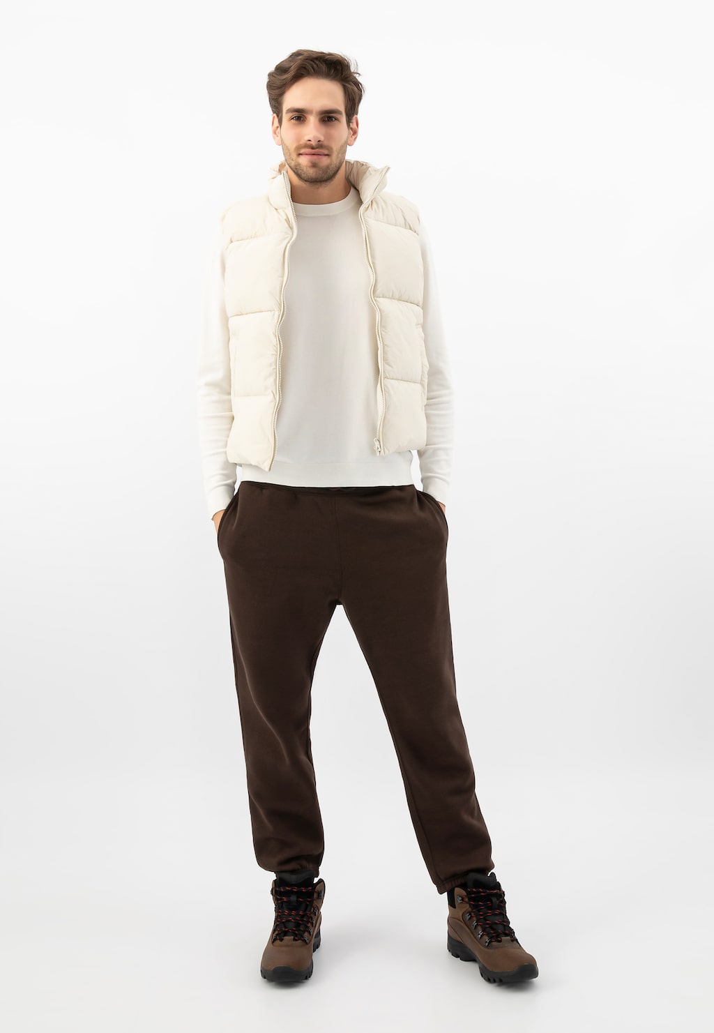 Osoba w białej puchowej kamizelce i swetrze, brązowych spodniach, prezentująca brązowe męskie trzewiki trekkingowe Wojas model 24027-92 idealne na zimowe wędrówki.