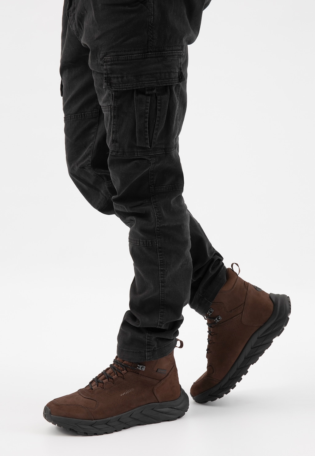 Brązowe wodoodporne trekkingi męskie Wojas 24113-72 z nubuku, prezentowane na nogach mężczyzny ubranego w czarne spodnie cargo, widok z boku.