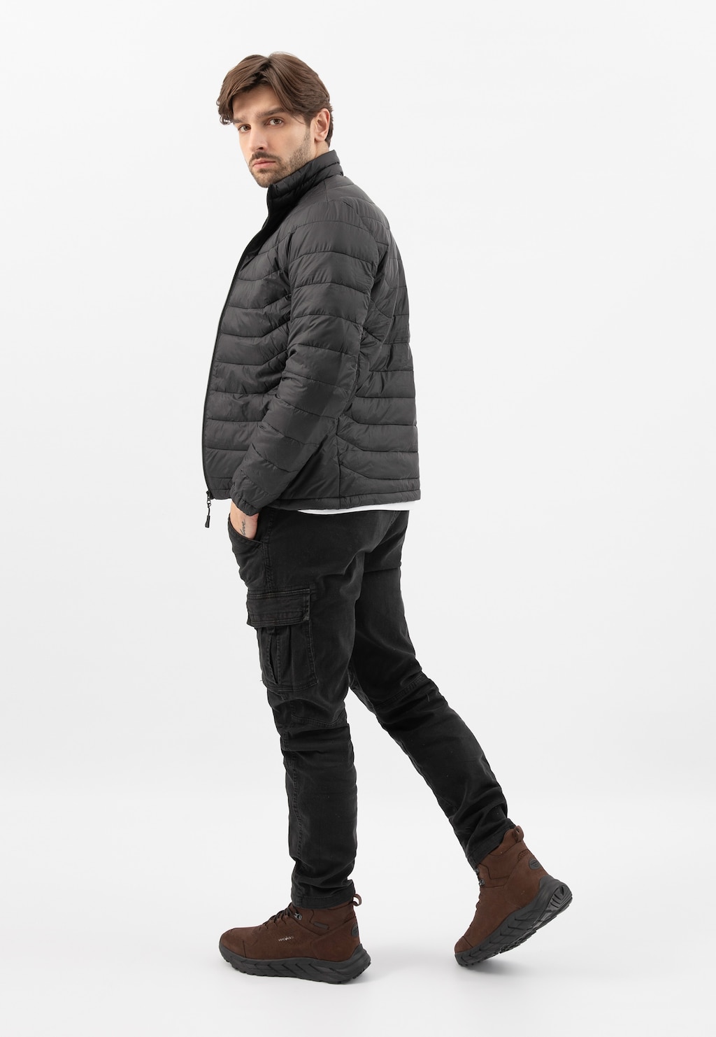 Model w zimowej stylizacji z brązowymi trekkingami Wojas 24113-72. Wodoodporne buty z nubuku doskonale uzupełniają outfit składający się z czarnej pikowanej kurtki i spodni cargo.