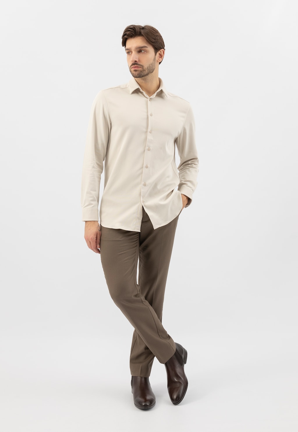 Model w eleganckiej stylizacji prezentuje ciemnobrązowe botki męskie Wojas 20041-52 ze skóry licowej, noszone z beżową koszulą i brązowymi spodniami.