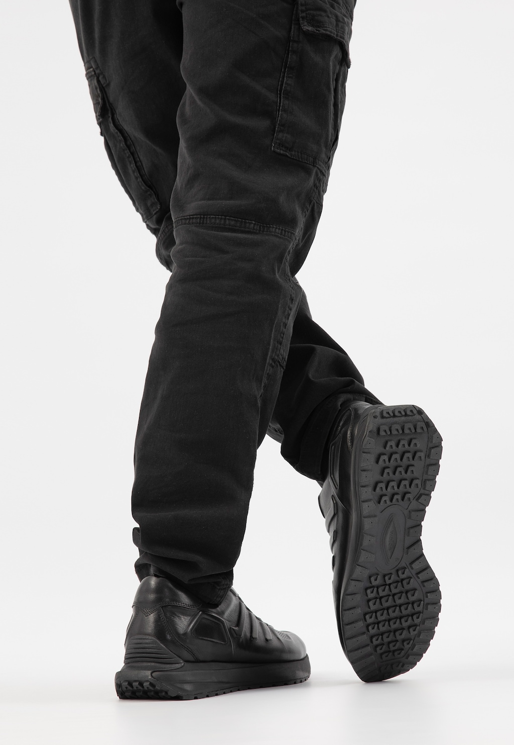 Czarne awangardowe sneakersy męskie Wojas model 10230-51 pokazane na nogach w czarnych spodniach cargo, widoczna charakterystyczna podeszwa z bieżnikiem.