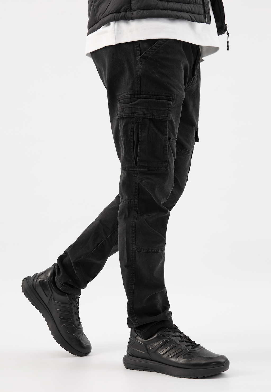 Czarne awangardowe sneakersy męskie Wojas 10230-51 widoczne na nogach osoby w czarnych spodniach cargo i białą koszulką pod czarną kurtką. Buty mają sportowy design i grubą podeszwę.
