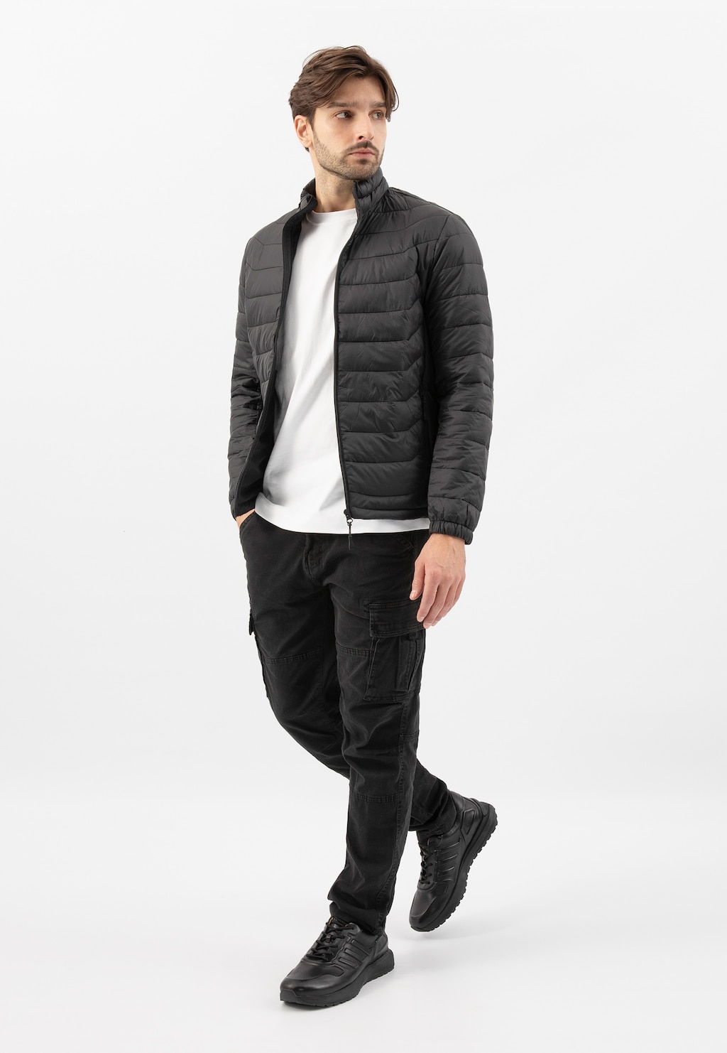 Osoba w czarnej pikowanej kurtce, białej koszulce i spodniach cargo, prezentująca czarne sneakersy Wojas model 10230-51 w eleganckim, awangardowym stylu.