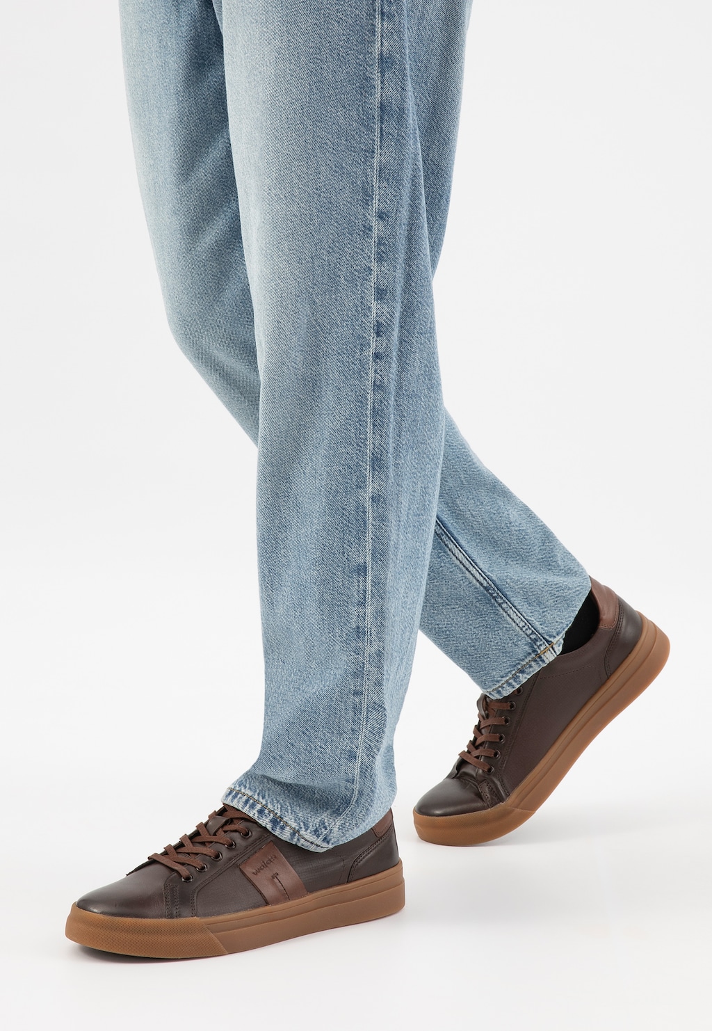 Brązowe trampki męskie Wojas model 10228-52 z jaśniejszymi wstawkami i gumową podeszwą, prezentowane na nogach w jasnych jeansach, widok z boku.