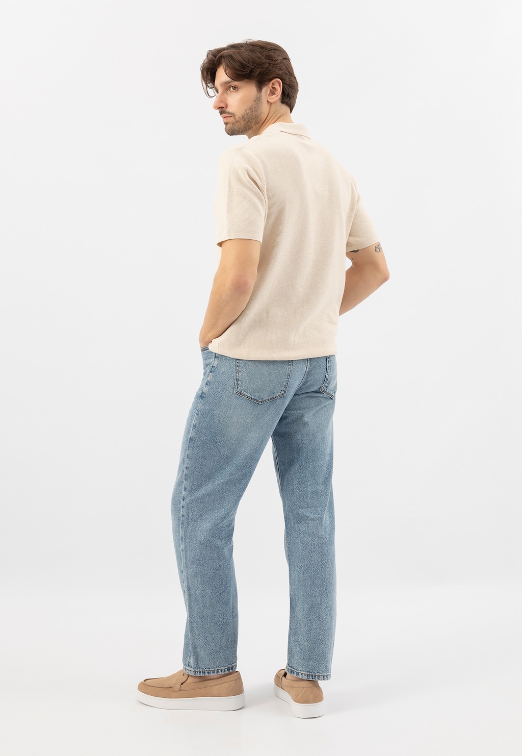 Osoba w beżowej koszulce i niebieskich jeansach, widoczna od tyłu, nosząca beżowe mokasyny męskie Wojas model 10218-64 na płaskiej białej podeszwie.