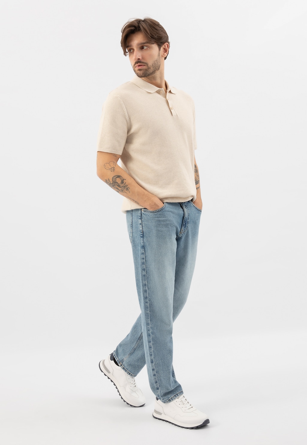 Osoba w jasnobeżowej koszulce polo i jasnoniebieskich jeansach prezentująca białe sneakersy męskie Wojas model 10201-50 z charakterystyczną kontrastową podeszwą.