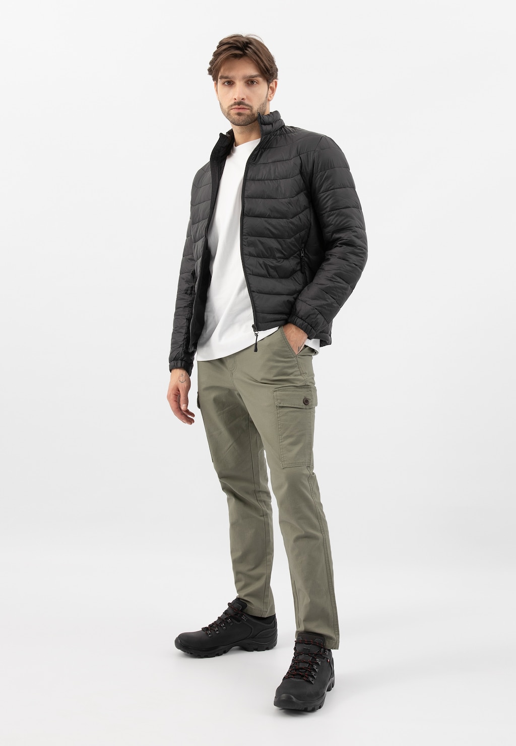 Model prezentuje czarne męskie półbuty Wojas 9377-91 w stylizacji z czarną pikowaną kurtką, białym t-shirtem i oliwkowymi spodniami cargo.