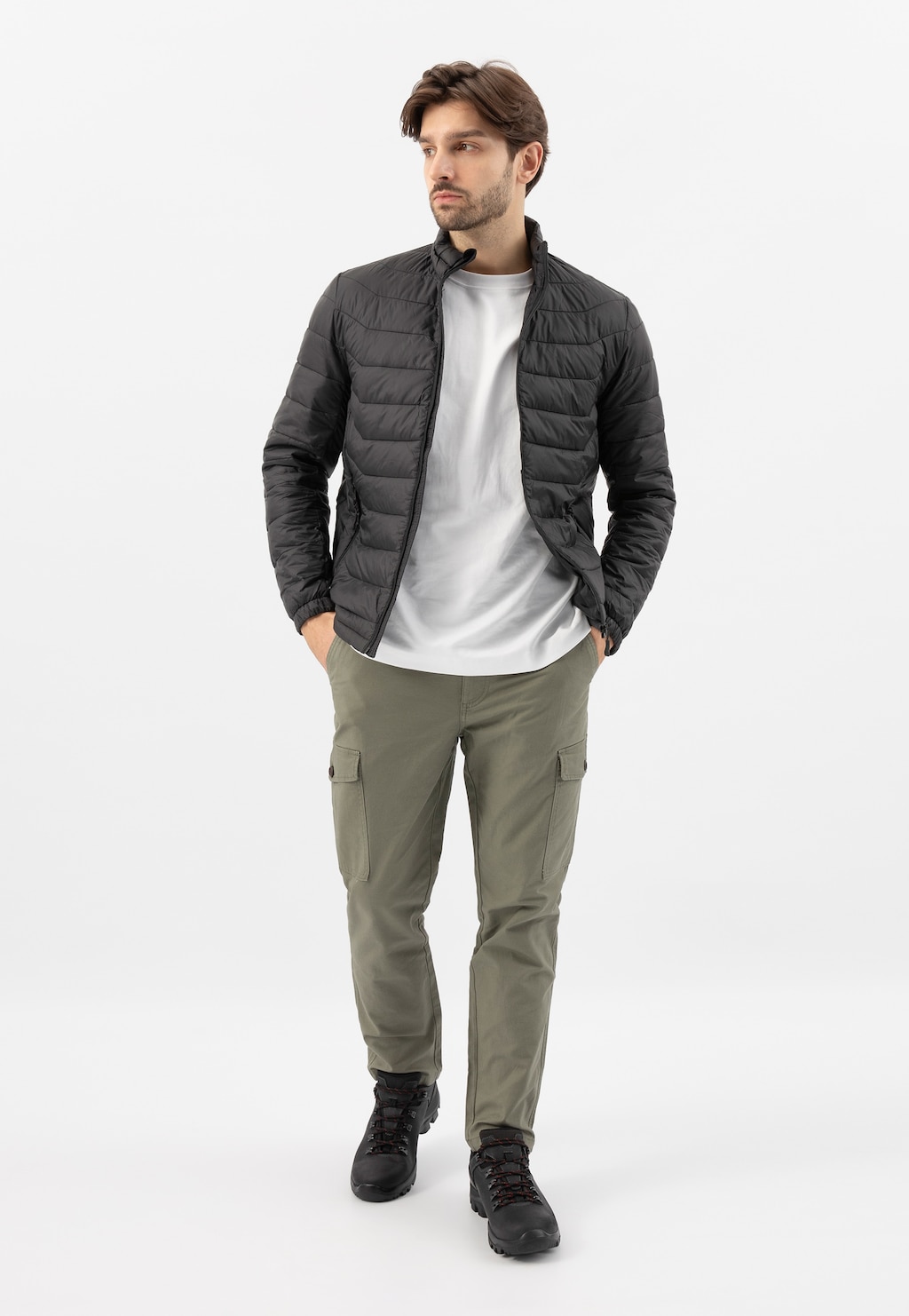 Model prezentuje czarne półbuty męskie Wojas 9377-91 w stylizacji z zieloną kurtką pikowaną, białym t-shirtem i spodniami typu cargo w kolorze oliwkowym.