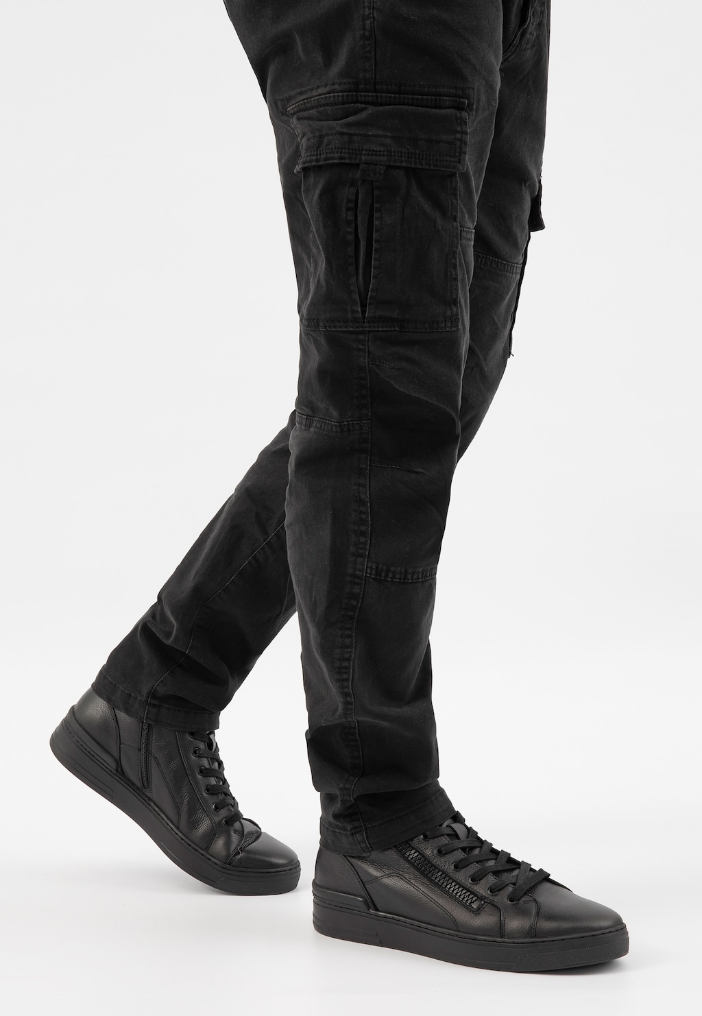 Czarne trzewiki męskie Wojas model 24083-51 z ozdobnym zamkiem bocznym, pokazane na nogach mężczyzny w czarnych spodniach cargo. Eleganckie buty na czarnej podeszwie.