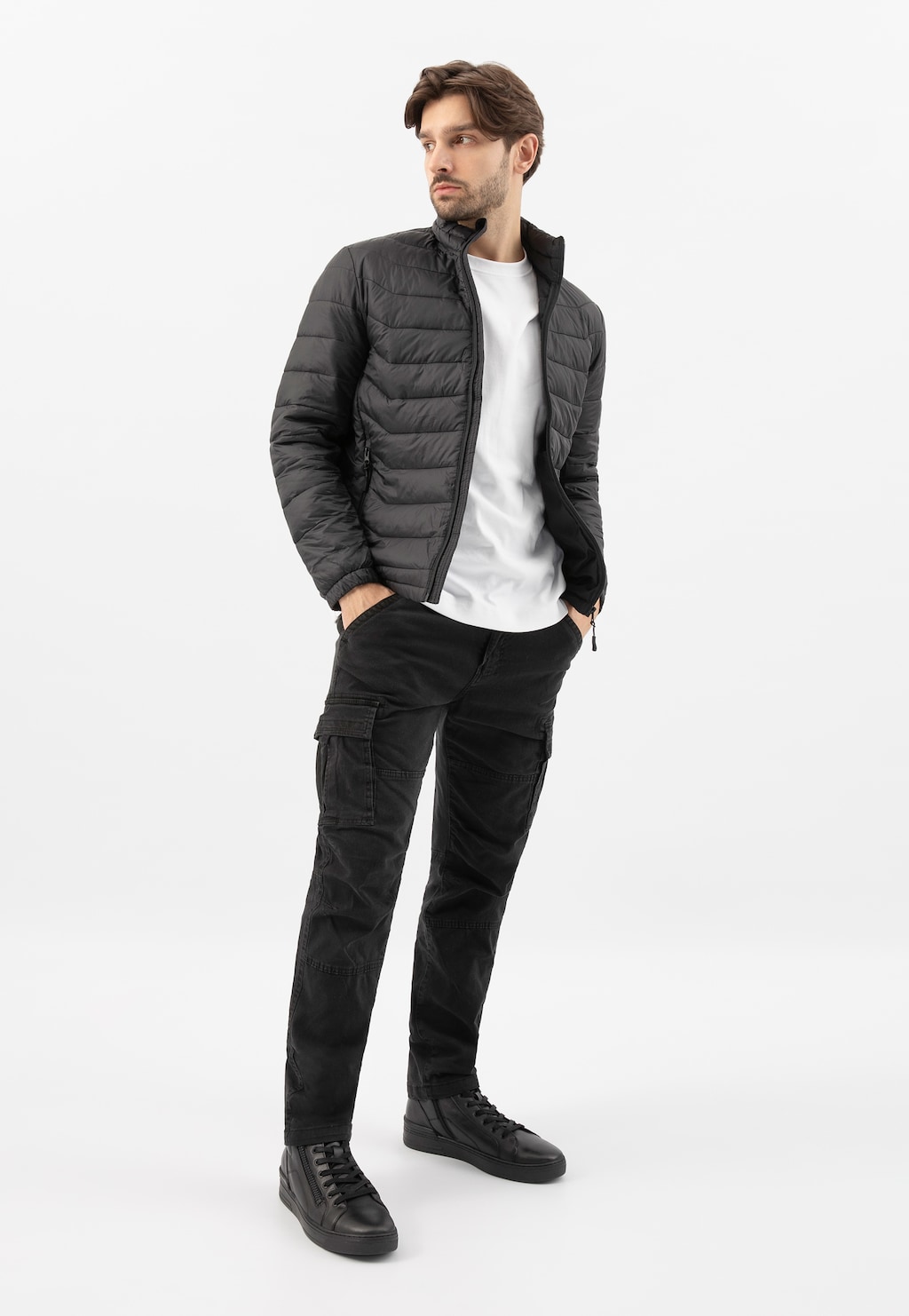 Model w czarnej pikowanej kurtce prezentuje trzewiki męskie Wojas 24083-51 z ozdobnym zamkiem. Stylizacja uzupełniona białym t-shirtem i czarnymi spodniami cargo.