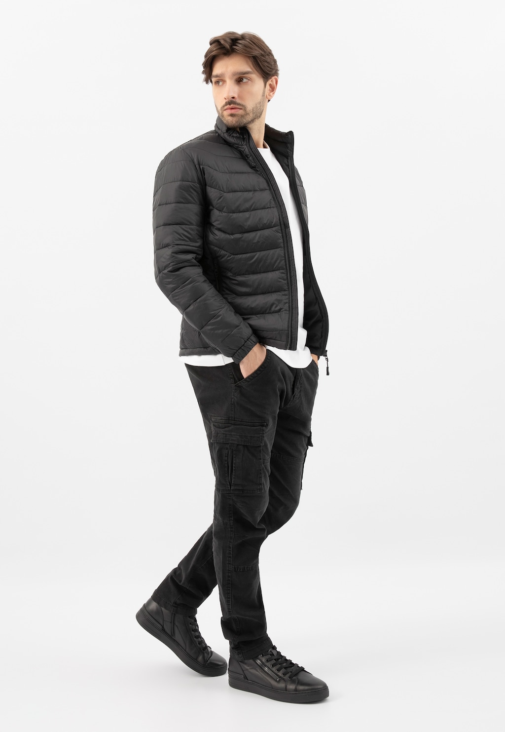 Model w czarnej puchowej kurtce i spodniach cargo prezentuje czarne trzewiki męskie Wojas model 24083-51 z ozdobnym zamkiem z boku.