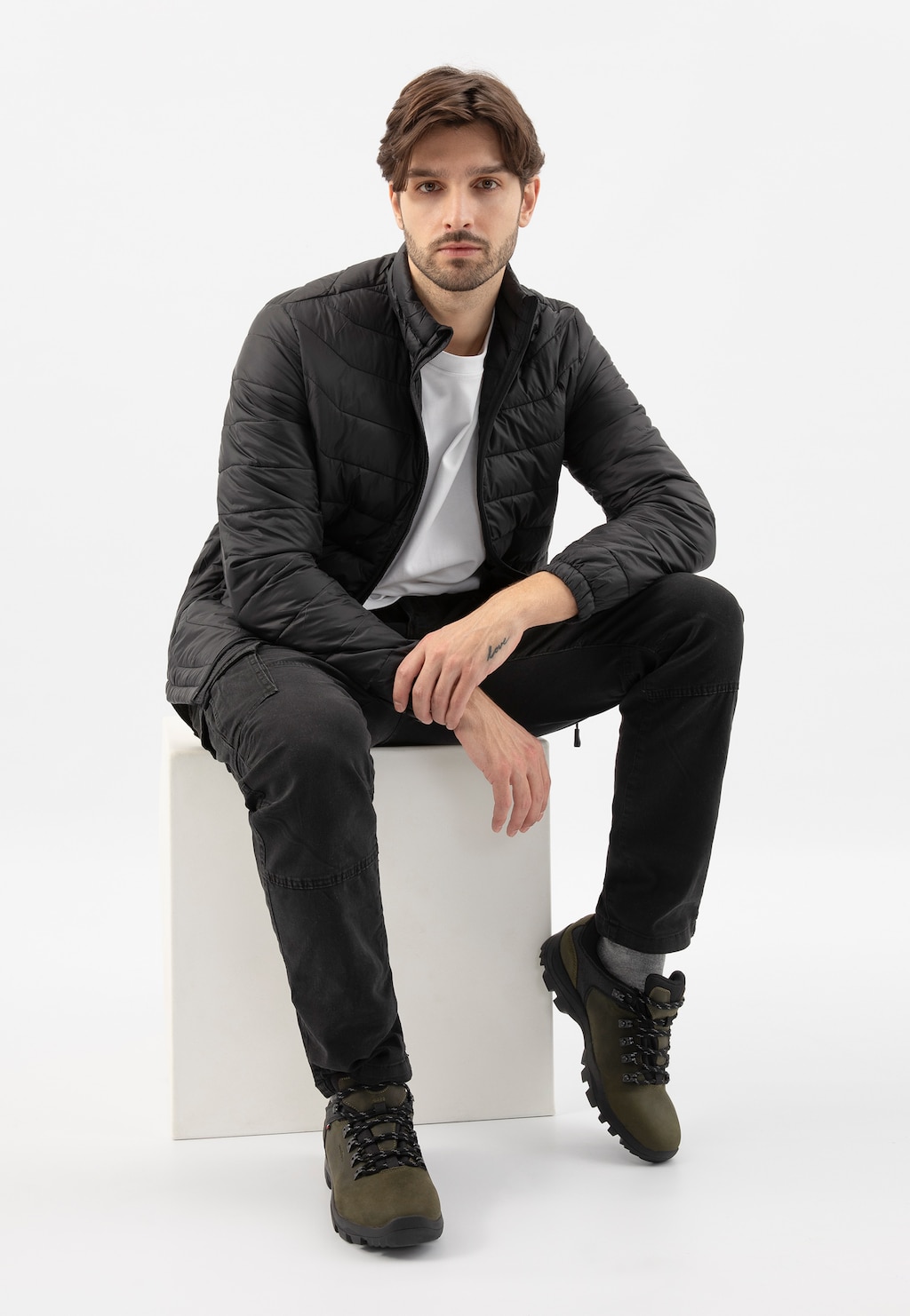 Zielono-czarne półbuty trekkingowe Wojas model 9377-87 prezentowane przez mężczyznę w czarnej kurtce i spodniach, siedzącego na białym postumencie.