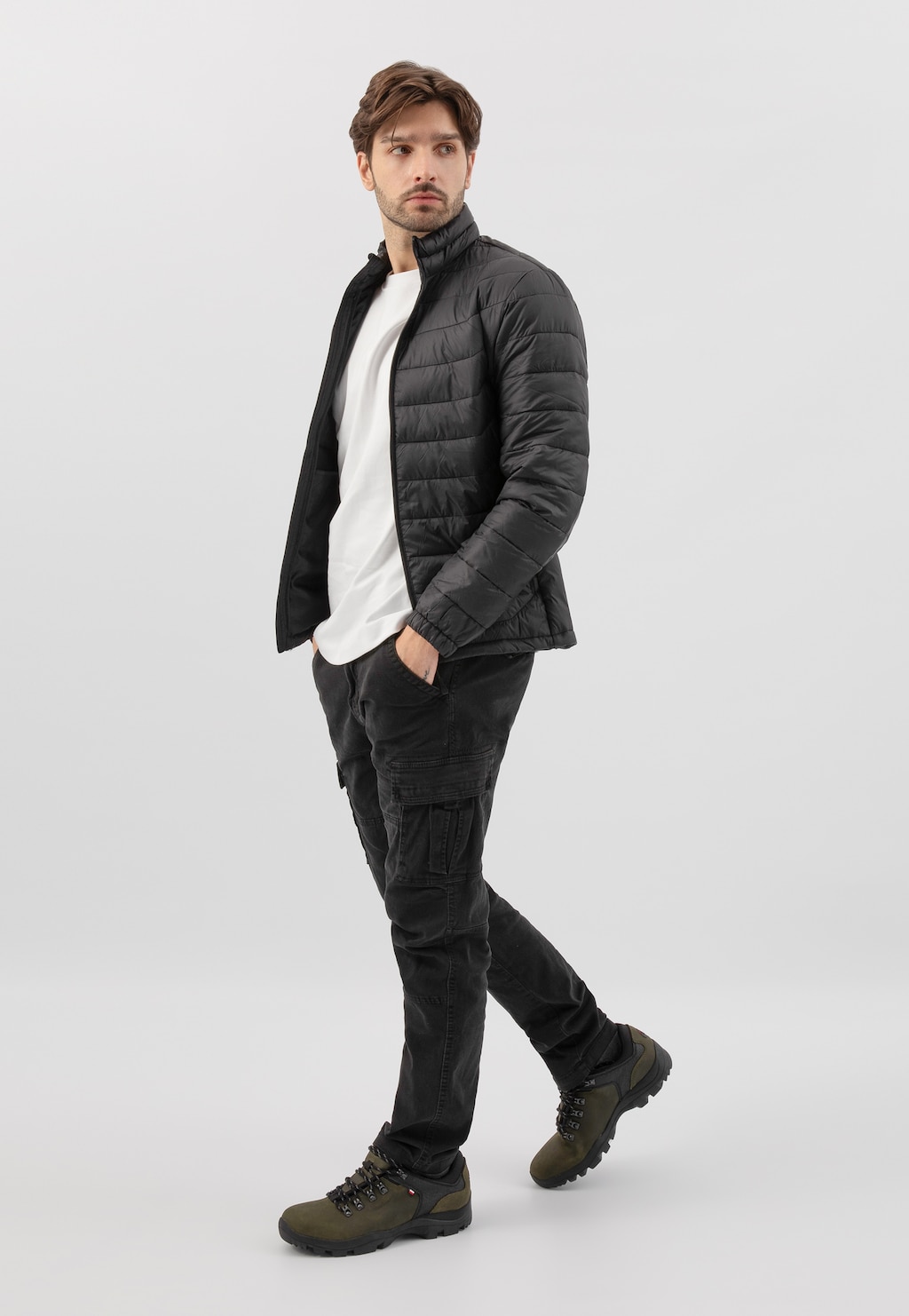 Model w czarnej pikowanej kurtce i spodniach cargo prezentuje zielono-czarne półbuty trekkingowe Wojas model 9377-87, idealne na górskie wędrówki.