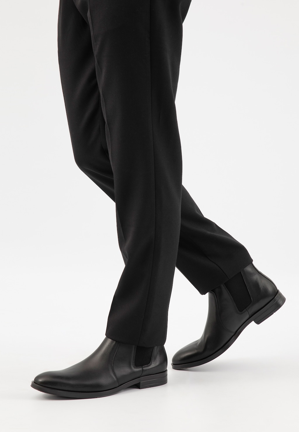 Eleganckie czarne sztyblety męskie Wojas model 20003-50 wykonane ze skóry licowej, noszone do czarnych spodni wizytowych, ukazane z profilu na nodze.