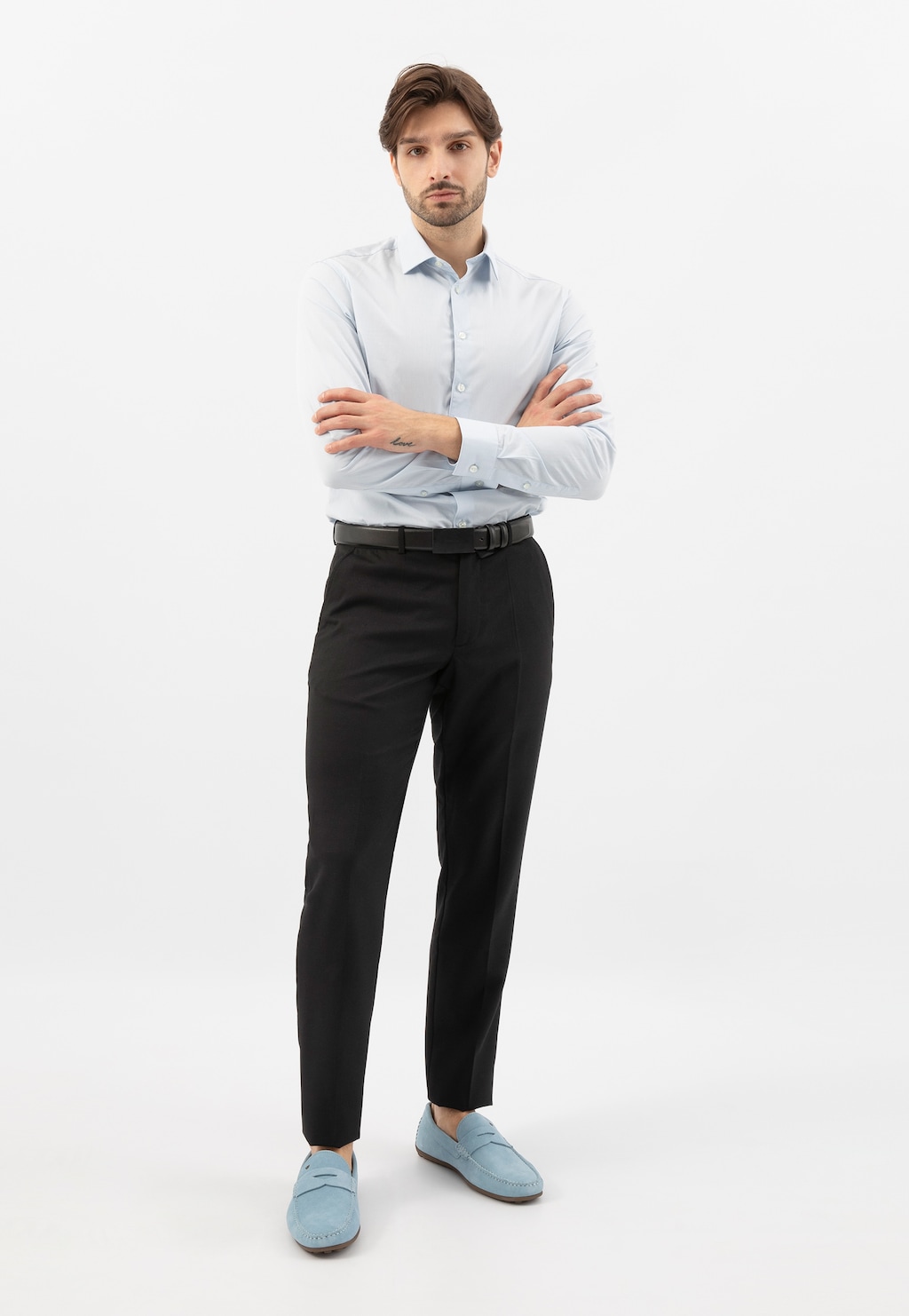 Model prezentujący niebieskie mokasyny męskie Wojas 10116-69 na wiosnę, ubrany w jasnoniebieską koszulę i czarne spodnie, stojący ze skrzyżowanymi ramionami.