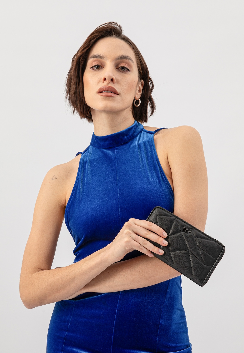 Osoba w niebieskiej sukience prezentująca czarny skórzany portfel Wojas model 91094-51 z geometrycznym pikowaniem i paskiem, elegancki dodatek do wieczorowej stylizacji.