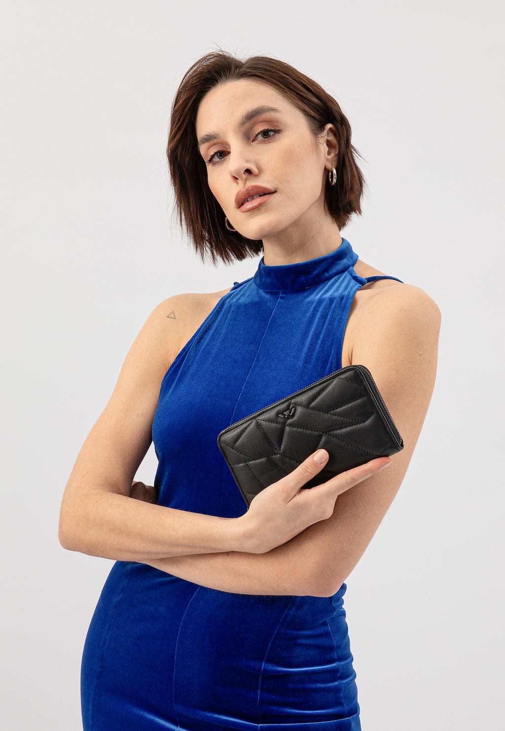 Elegancki czarny portfel Wojas 91094-51 z charakterystycznym geometrycznym pikowaniem i paskiem, prezentowany w dłoni na tle kobiety w niebieskiej sukience.