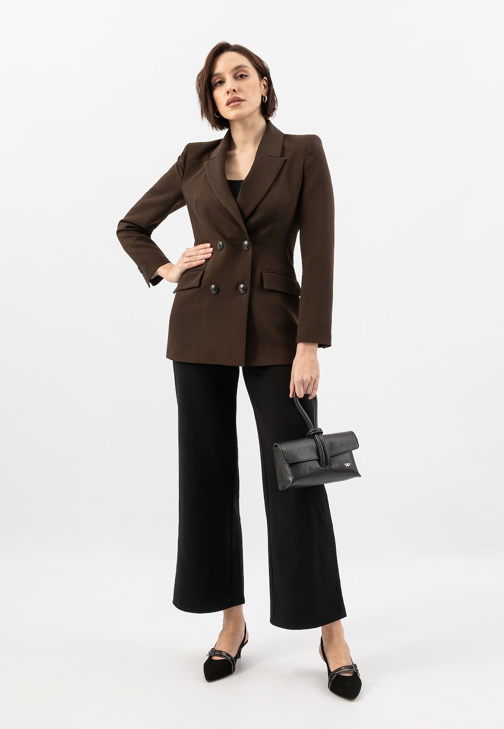 Modelka w brązowej marynarce i czarnych spodniach trzymająca czarną wizytową torebkę skórzaną Wojas model 80430-51, uzupełniona eleganckimi butami.