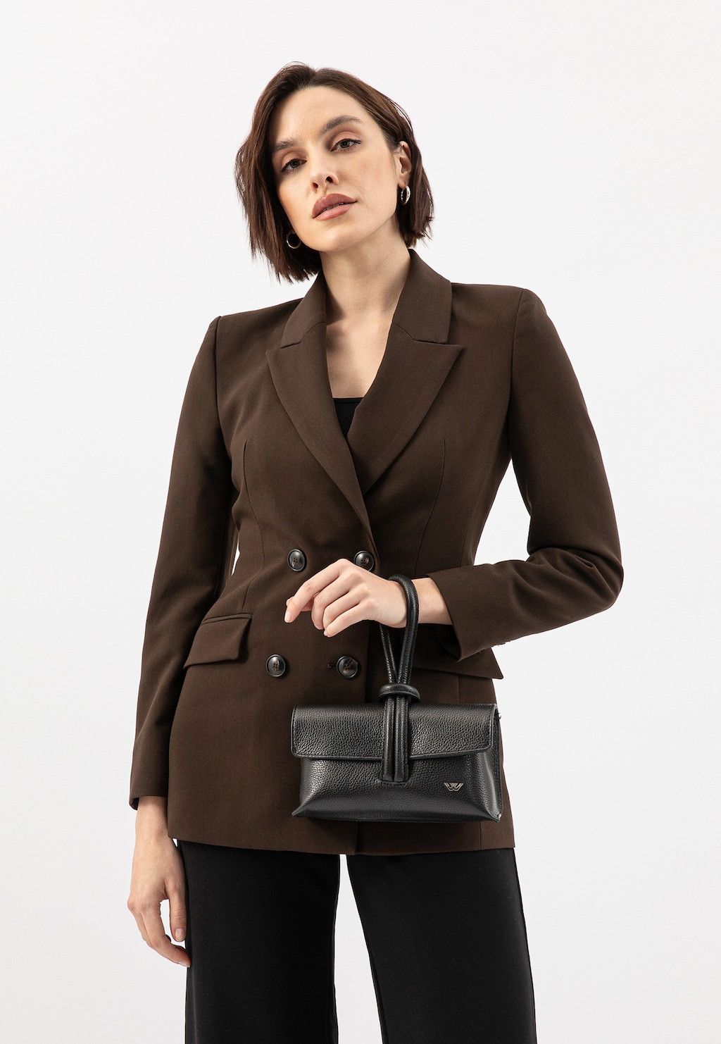 Modelka w brązowej marynarce trzymająca elegancką czarną torebkę Wojas model 80430-51, prezentowaną z przodu. Stylowy dodatek do wizytowej stylizacji biznesowej.