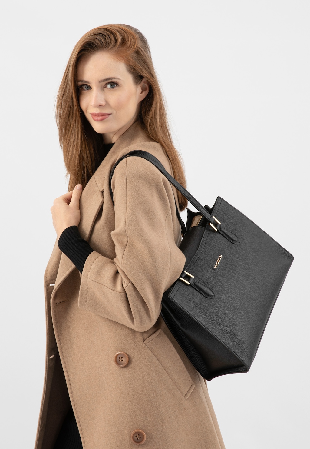 Elegancki czarny skórzany kuferek Wojas model 80410-51 ze złotymi elementami noszony na ramieniu, prezentowany z beżowym płaszczem w stylu biznesowym.