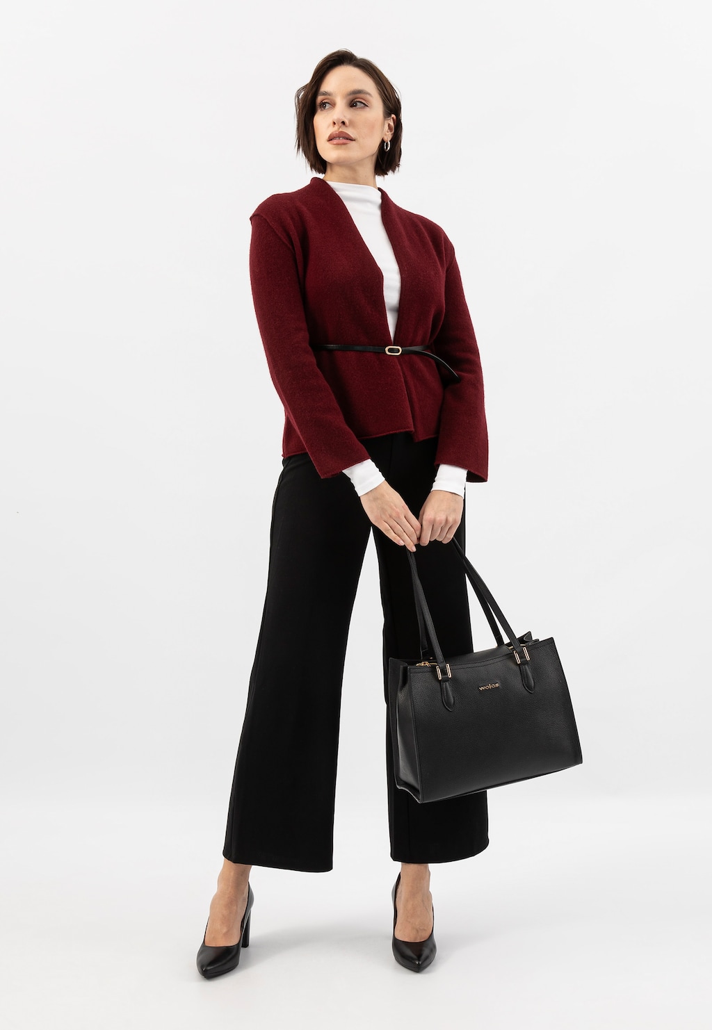 Modelka w eleganckim stroju z bordowym żakietem i czarnymi spodniami, trzymająca czarny skórzany kuferek Wojas model 80410-51 ze złotymi elementami.