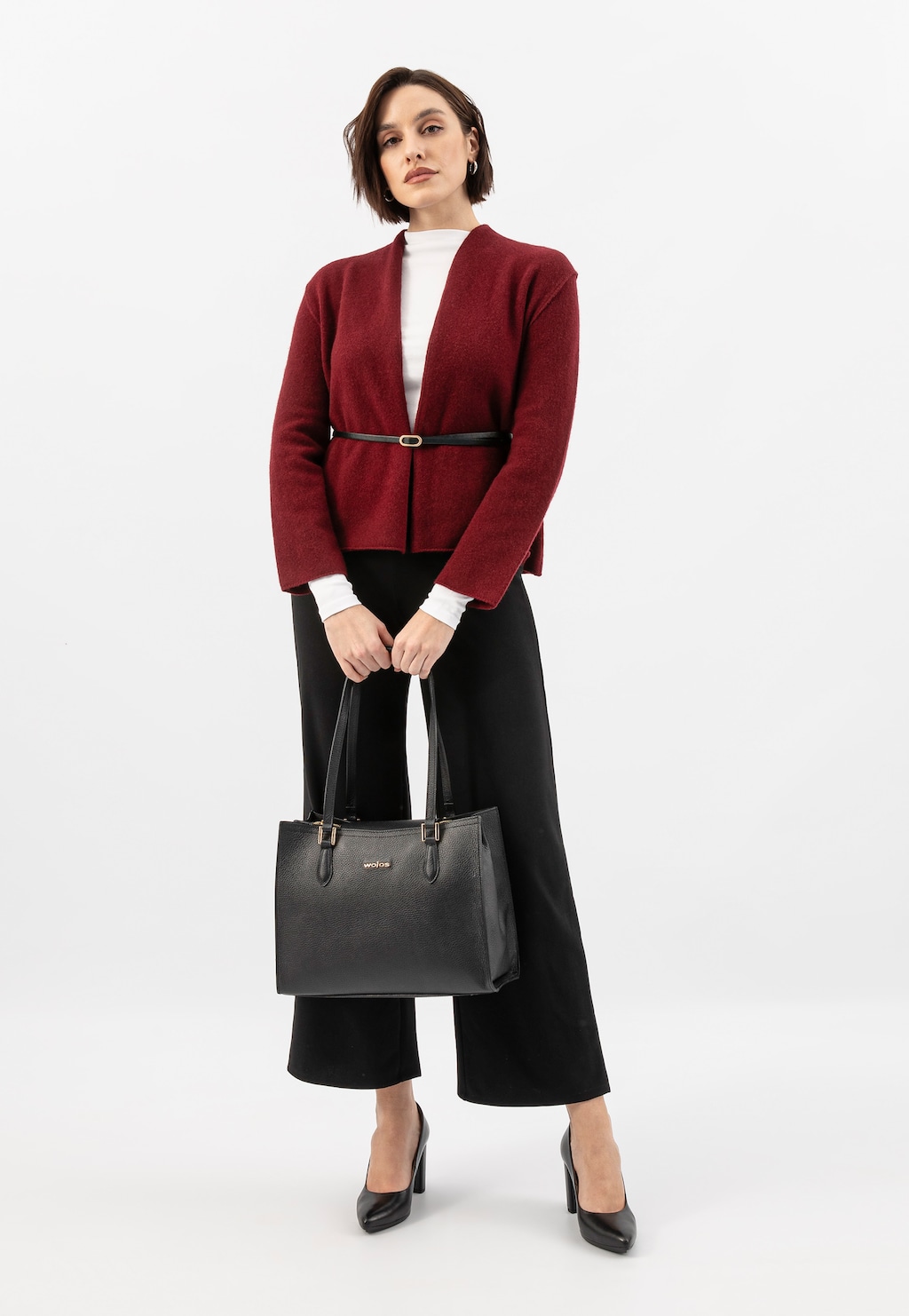 Elegancka stylizacja z burgundowym żakietem, czarnymi spodniami i czarnym skórzanym kuferkiem Wojas 80410-51 ze złotymi elementami, prezentowana z czarnymi szpilkami.