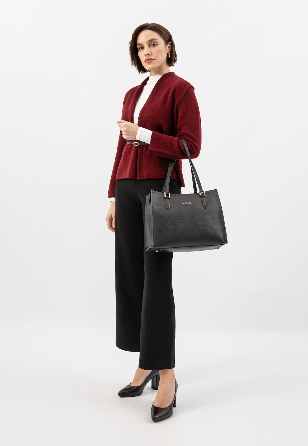 Elegancki czarny skórzany kuferek Wojas model 80410-51 ze złotymi elementami, prezentowany w stylizacji z bordowym kardiganem, białą bluzką i czarnymi spodniami.