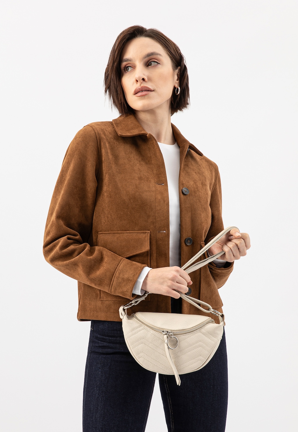 Modelka w brązowej zamszowej kurtce trzymająca beżową pikowaną saszetkę damską Wojas model 80093-54 ze skóry licowej, z regulowanym paskiem i ozdobnym suwakiem.