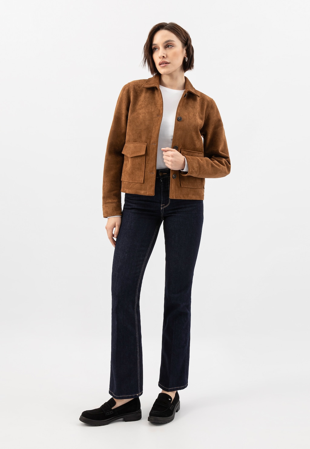 Modelka w stylizacji z brązową zamszową kurtką, białym topem i jeansami, prezentująca czarne mokasyny damskie Wojas model 46301-61 z dwoiny welurowej.