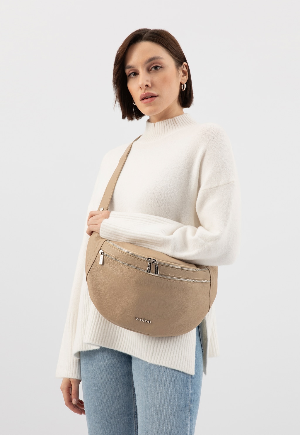 Beżowa skórzana torebka nerka Wojas model 80298-54 prezentowana na osobie w białym swetrze i jasnoniebieskich jeansach. Torebka ma praktyczne zamki i elegancki minimalistyczny design.