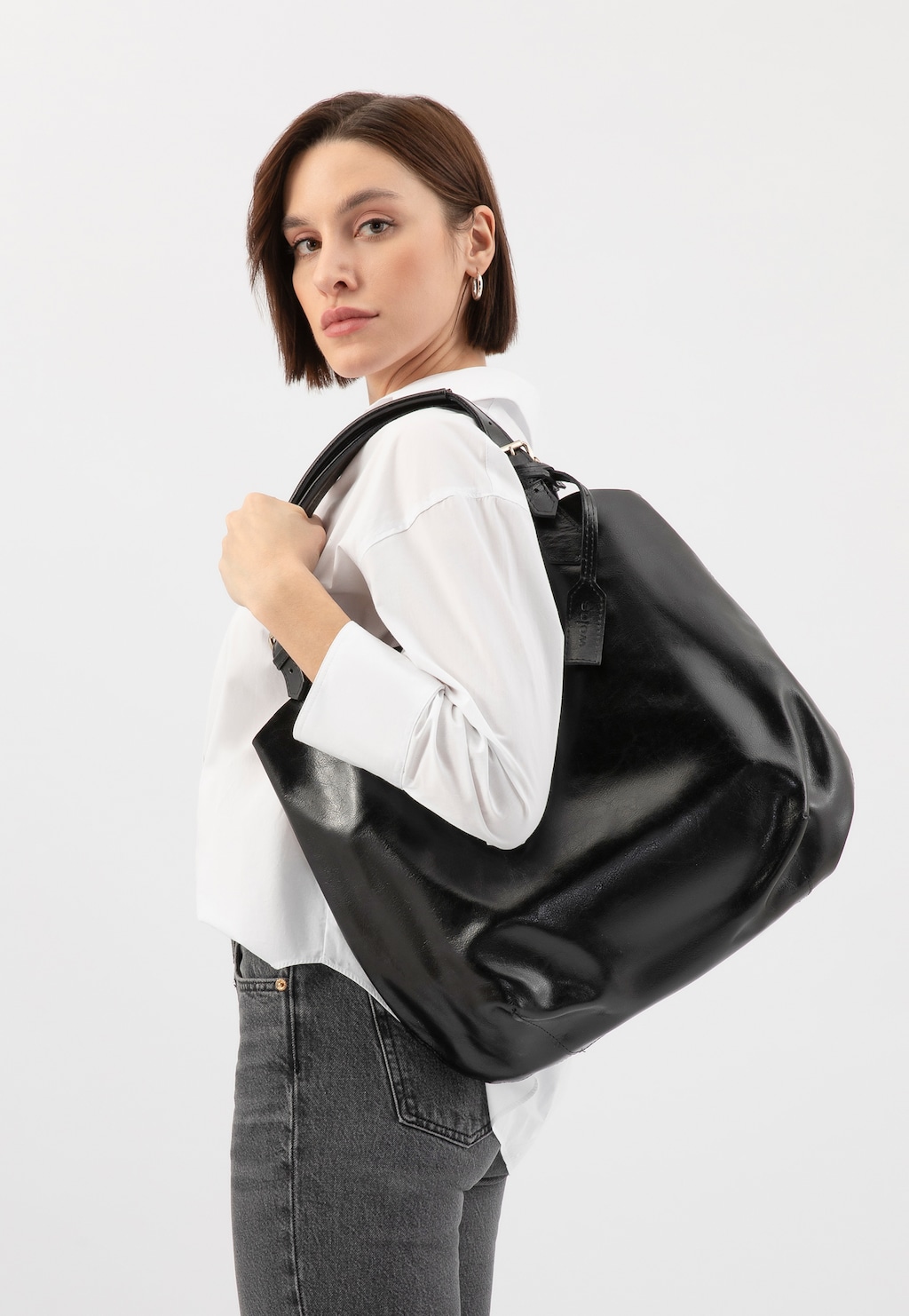 Modelka w białej koszuli prezentuje czarną, dużą shopperką damską Wojas model 80205-51, niesioną na ramieniu. Torebka wyróżnia się pojemnym wnętrzem i eleganckim wykończeniem.