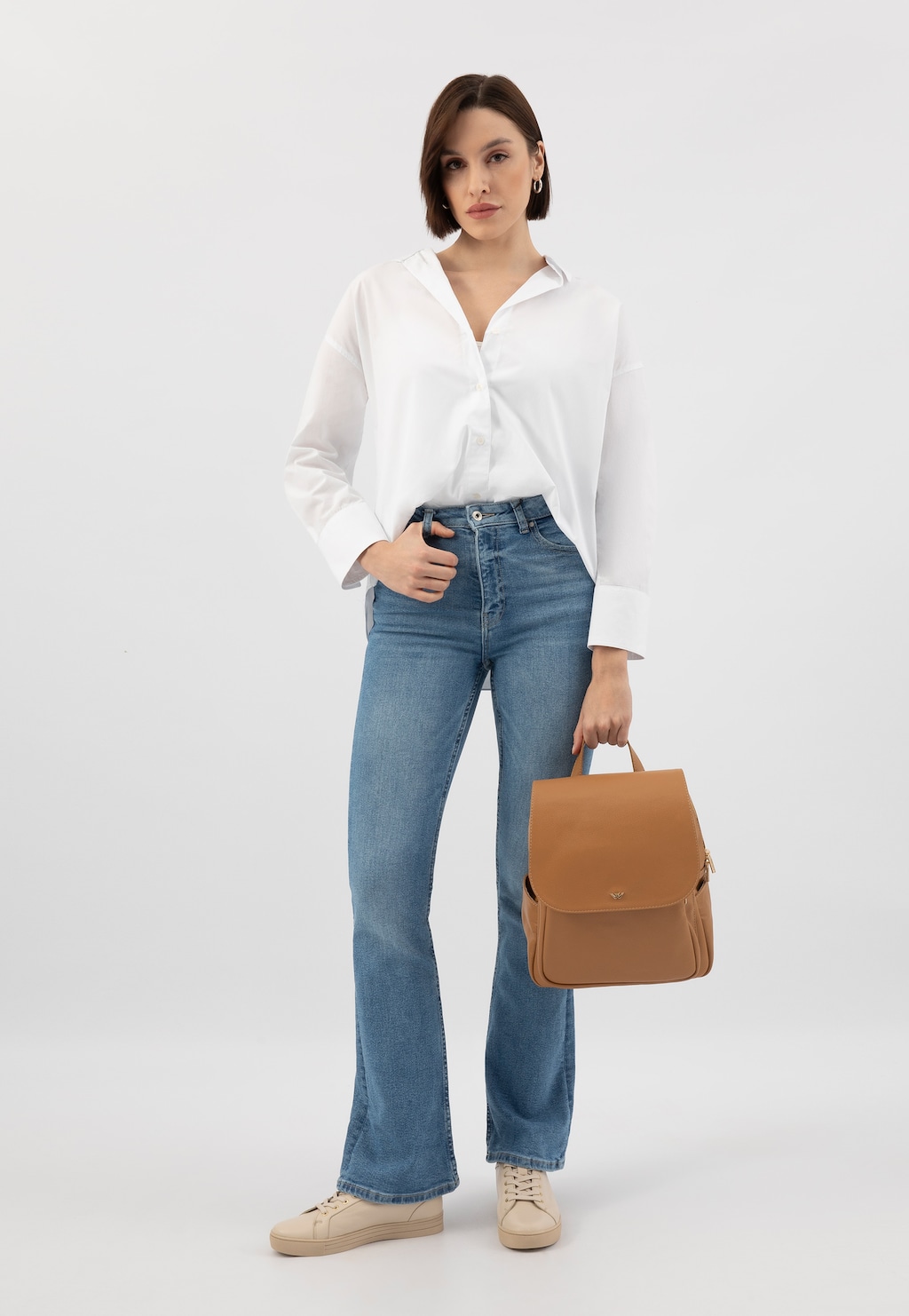 Elegancki beżowy skórzany plecak miejski Wojas 80082-54 prezentowany z białą koszulą i jeansami. Funkcjonalny design z klapką idealny do codziennych stylizacji.