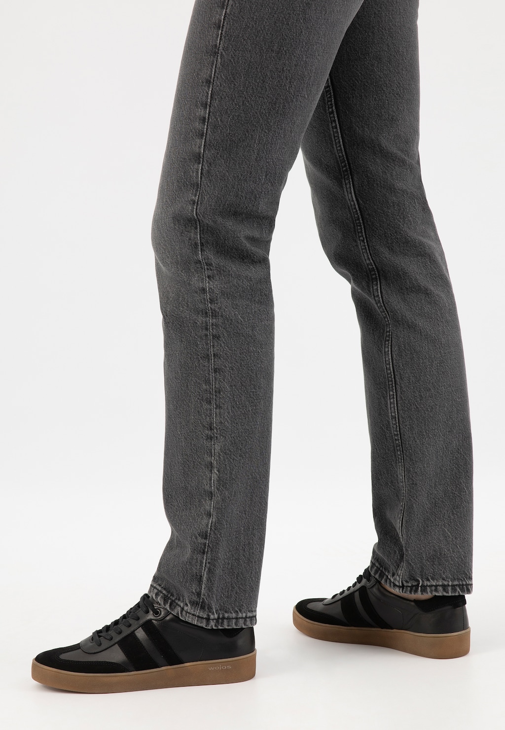 Czarne płaskie trampki Wojas model 46307-71 z łączonych skór, widoczne na nogach w szarych jeansach. Buty mają gumową podeszwę w kolorze brązowym.