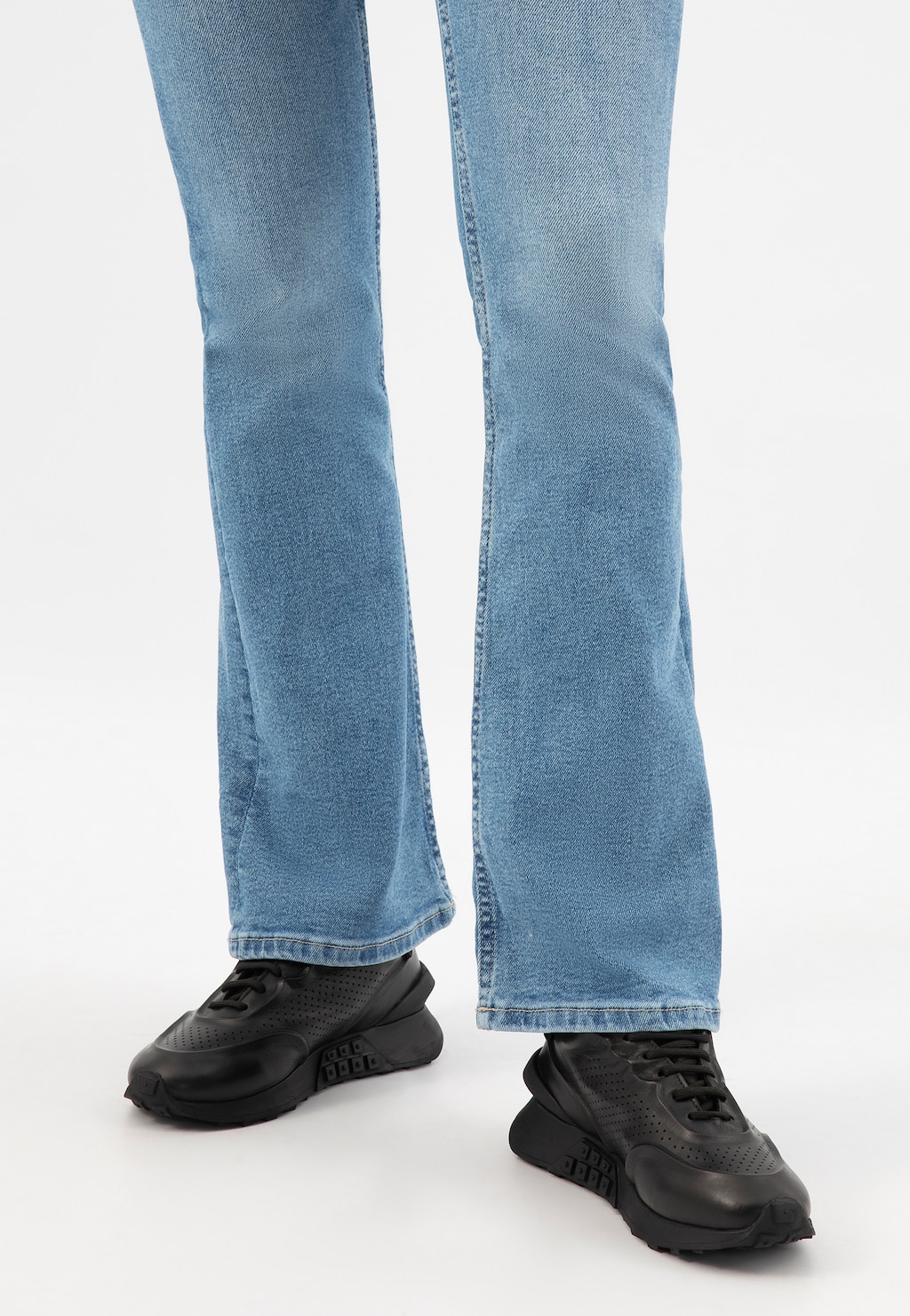 Czarne skórzane sneakersy damskie Wojas model 46306-51 noszone do jasnoniebieskich jeansów typu straight. Widok od dołu ukazujący perforowany wzór na butach.