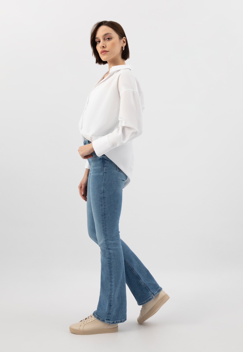 Modelka w białej koszuli i jeansach prezentująca beżowe trampki Wojas model 46019-54 ze złotymi akcentami. Buty widoczne w całej stylizacji z profilu.