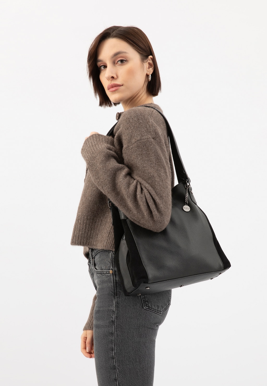 Modelka w brązowym swetrze i jeansach prezentuje dużą czarną torebkę damską skórzaną Wojas model 9859-71, przewieszoną przez ramię.