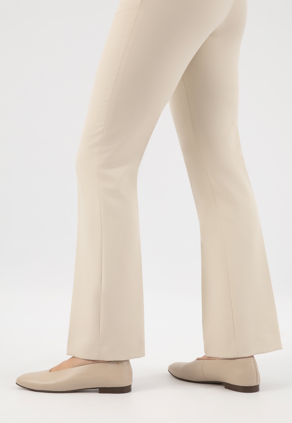 Beżowe baleriny Wojas model 44030-54 ze skóry licowej na niskim obcasie, widoczne od tyłu na nogach w jasnych spodniach rozszerzanych ku dołowi.