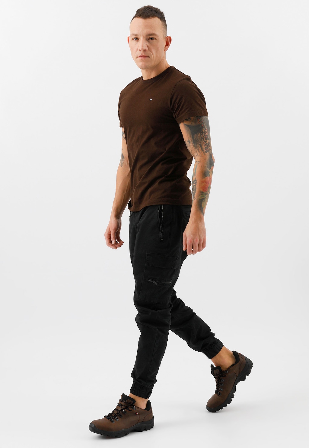 Mężczyzna w brązowym t-shircie i czarnych spodniach prezentujący brązowe męskie półbuty trekkingowe Wojas model 9377-92, widoczne podczas chodu z profilu.