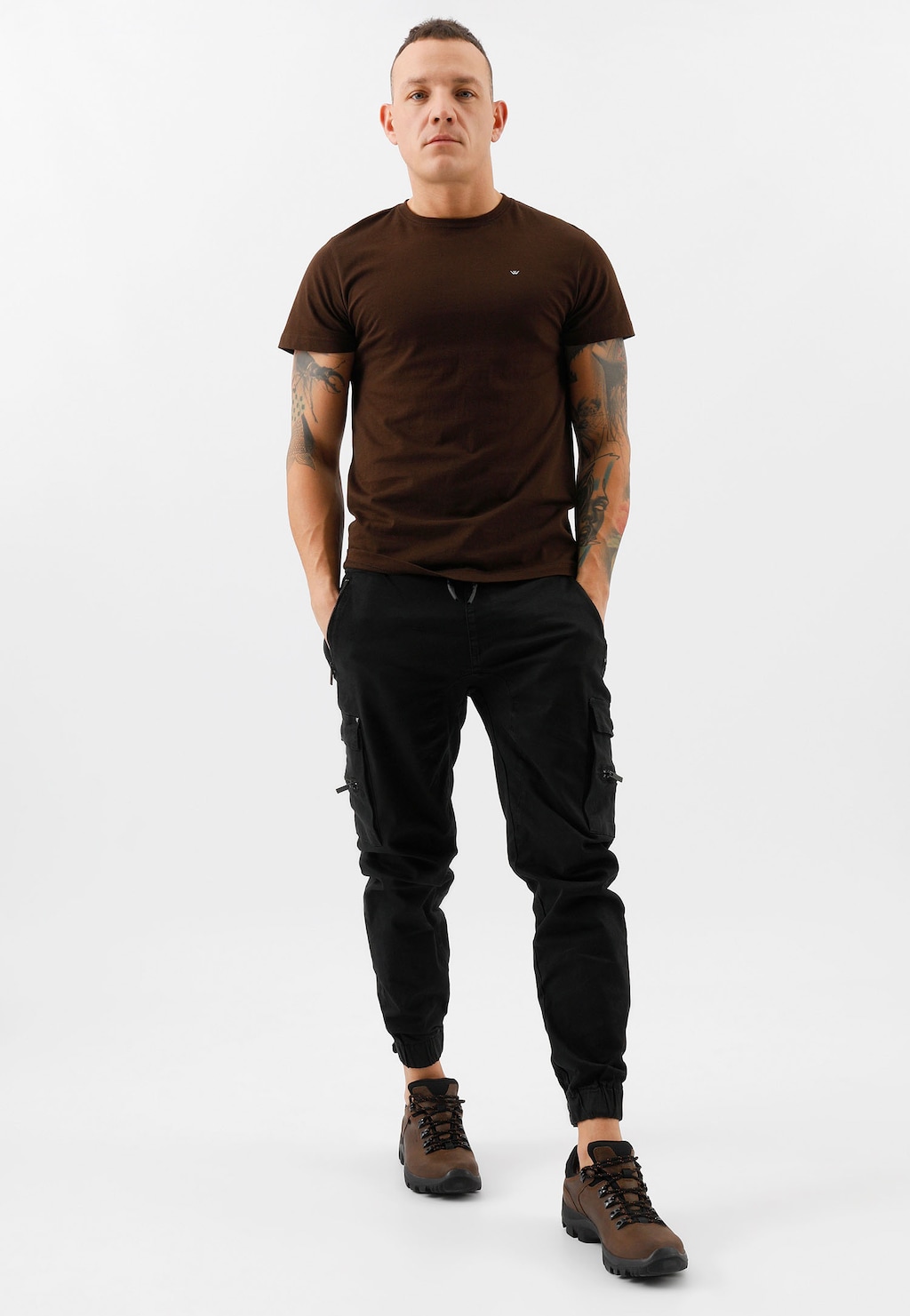 Osoba w brązowym t-shircie i czarnych spodniach cargo, prezentująca brązowe męskie półbuty trekkingowe Wojas model 9377-92 na jasnym tle.