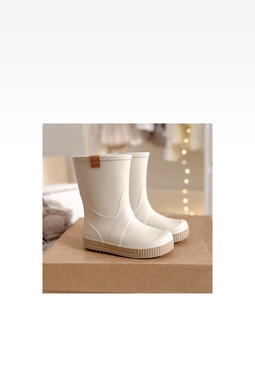 Beżowe gumowe kalosze dziecięce BARTEK model 86699-14 z brązowym logo, ustawione na kartonowym podłożu, z jasnym wnętrzem pokoju w tle.