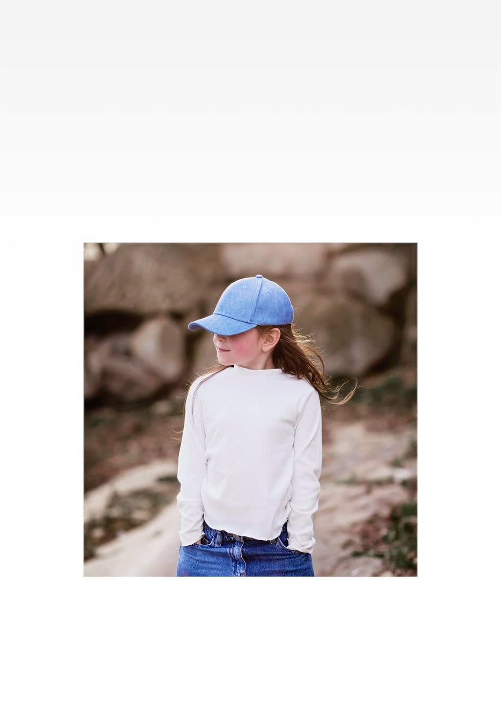 Dziecko w białej bluzie prezentujące niebieską jeansową czapkę z daszkiem marki Bartek model 85610-16, widok od tyłu w naturalnym otoczeniu.