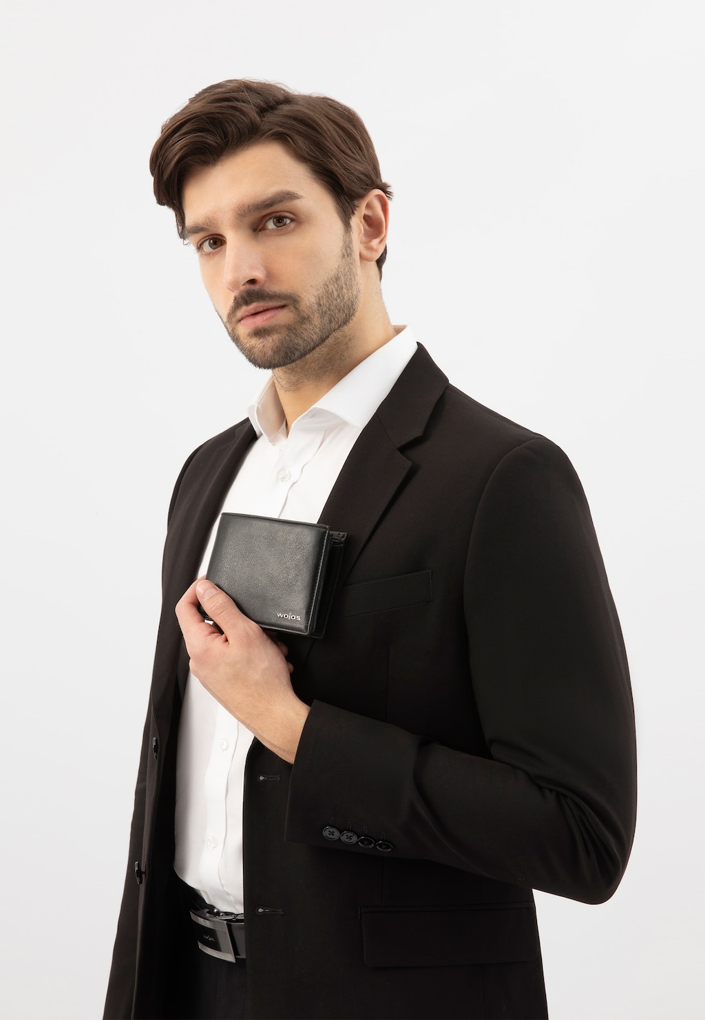 Elegancki czarny skórzany portfel męski Wojas model 8938-51 z metalowym logo, prezentowany przez osobę w ciemnym garniturze i białej koszuli.