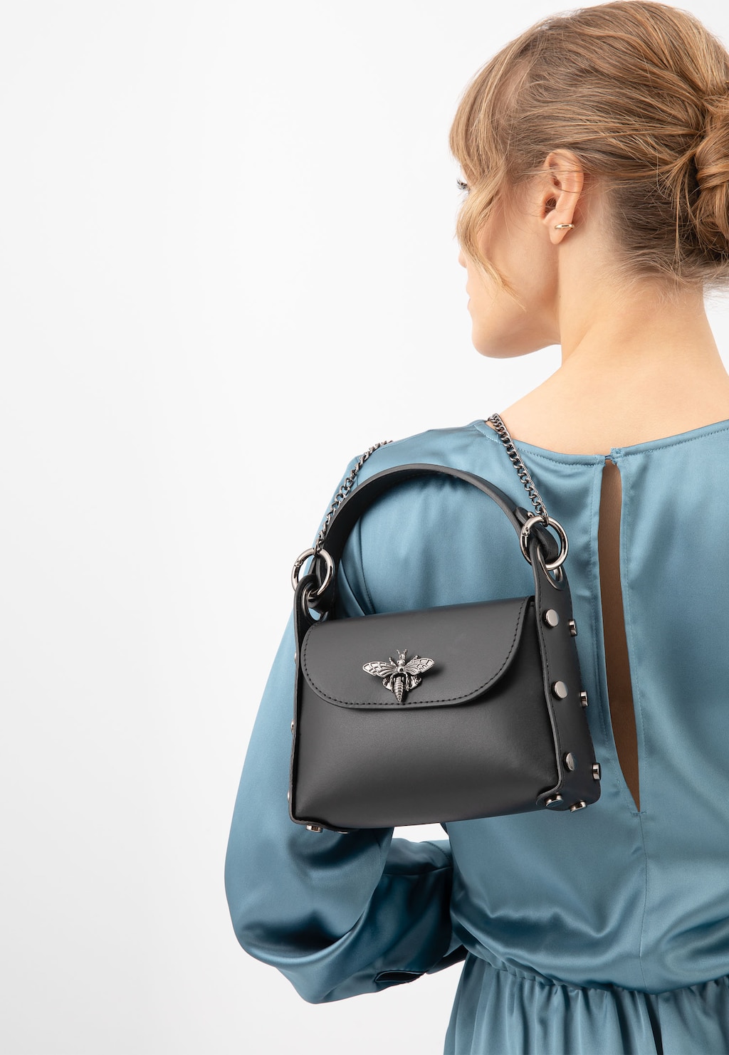 Czarna elegancka torebka wizytowa Wojas 80318-51 na ramieniu osoby w błękitnej sukience. Torebka zdobiona ozdobą w kształcie pszczoły i metalowym łańcuszkiem.