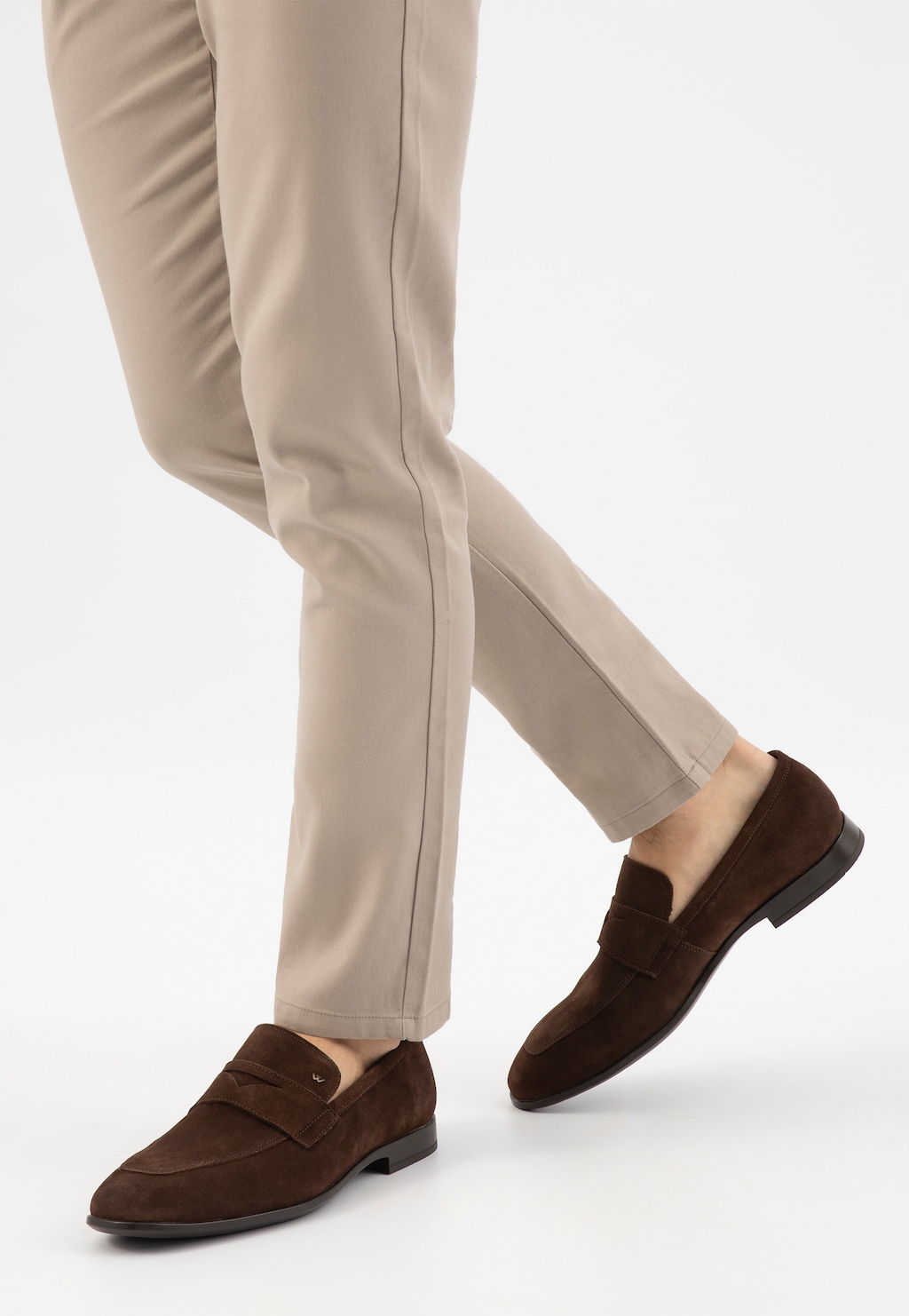 Brązowe loafersy męskie Wojas model 10196-62 z dwoiny welurowej, prezentowane na nogach w beżowych spodniach. Eleganckie buty w stylu penny loafer z charakterystycznym paskiem.