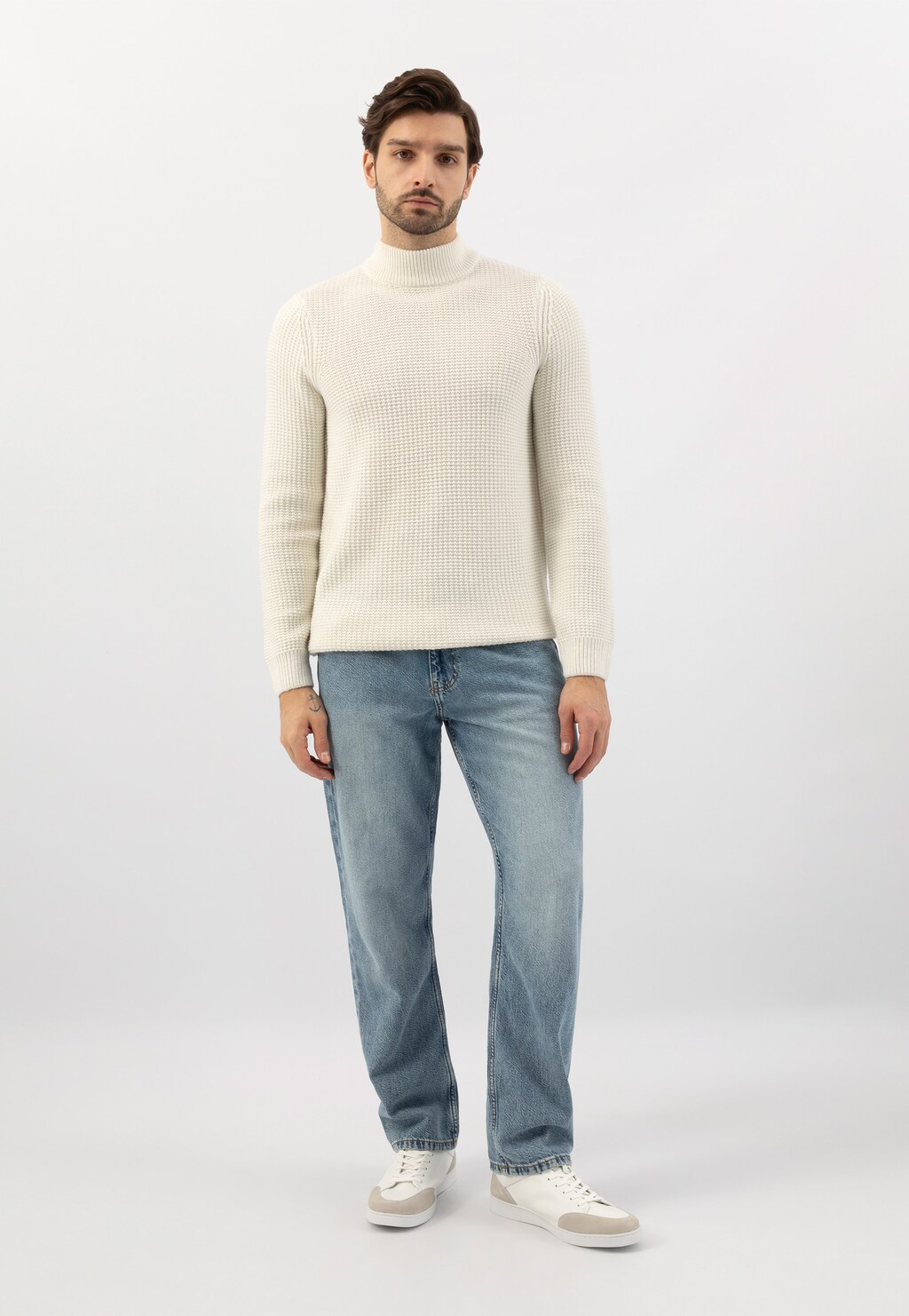 Osoba w białym golfie i jasnoniebieskich jeansach prezentująca białe trampki męskie Wojas z szarymi wstawkami model 10217-50, widoczne w całej stylizacji.