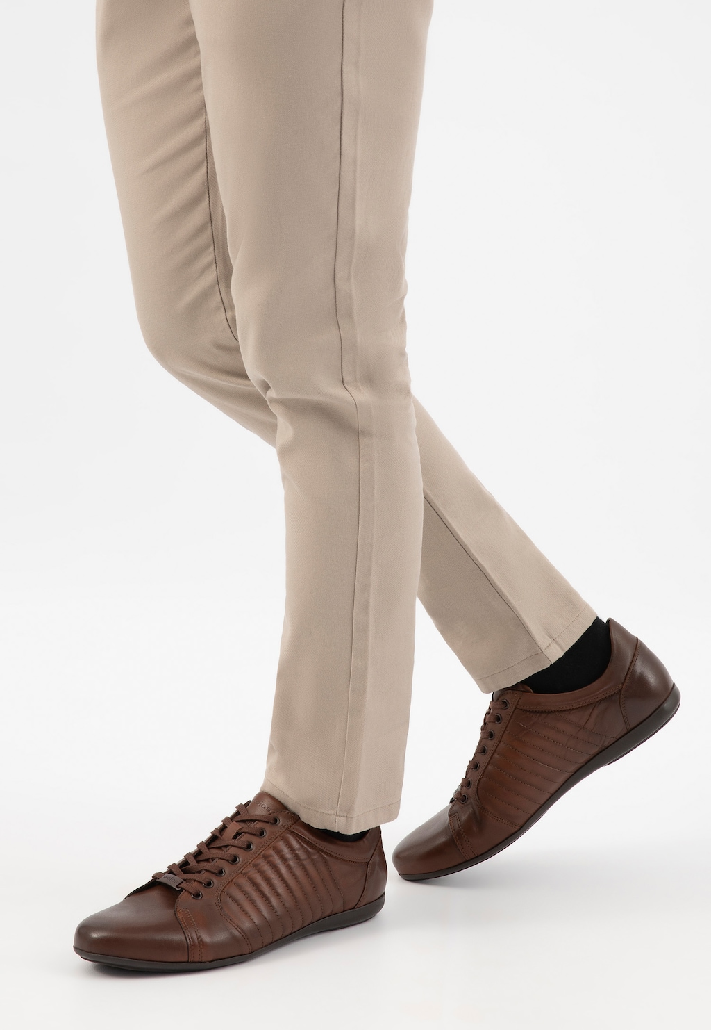 Brązowe skórzane sneakersy męskie Wojas model 10240-52 z charakterystycznymi przeszyciami, prezentowane na nogach w jasnych spodniach, widok z perspektywy bocznej.