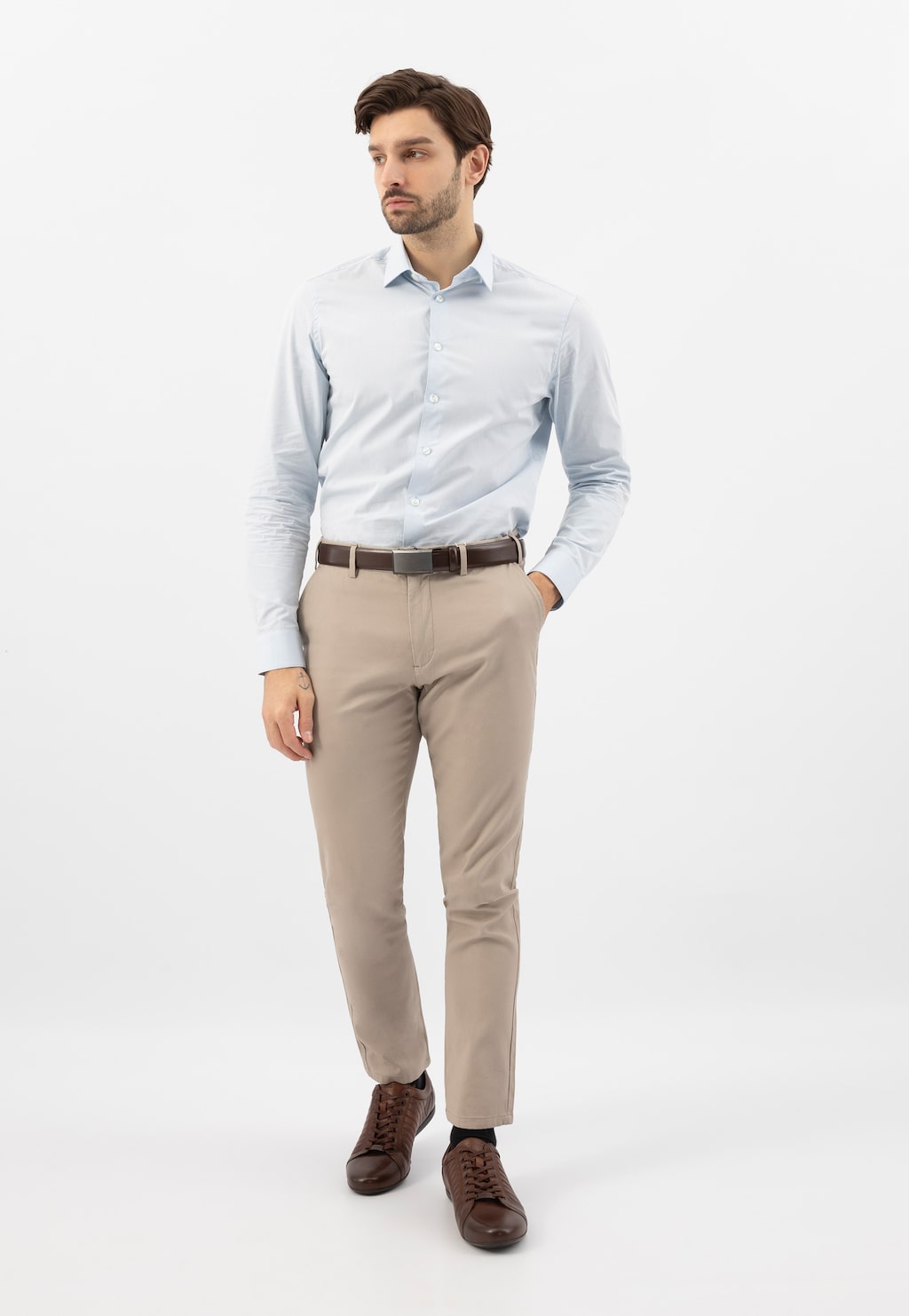 Model w eleganckiej stylizacji prezentuje brązowe skórzane sneakersy Wojas 10240-52 z charakterystycznymi przeszyciami, noszone do jasnej koszuli i beżowych spodni.