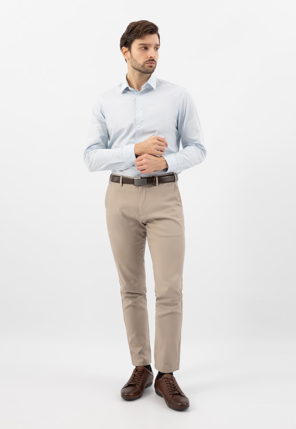 Model w eleganckim stroju z brązowymi skórzanymi sneakersami Wojas 10240-52. Męskie buty z charakterystycznymi przeszyciami idealnie uzupełniają stylizację z błękitną koszulą i beżowymi spodniami.